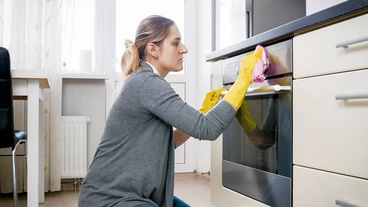 年轻疲倦的主妇在乳胶手套清洁烤箱在厨房