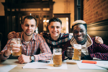 多种族的朋友团体在酒吧喝酒和敬酒啤酒。友谊概念与年轻人一起享受时间在一起和有乐趣