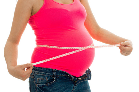 密切的孕妇在粉红色的衬衫测量她的肚子联系孤立在白色背景上的磁带