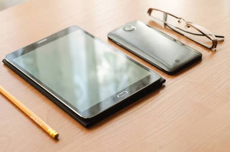 桌上躺着的眼镜和一款平板电脑 智能手机和一支铅笔
