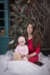圣诞晚会。母亲和女儿坐在椅子上的壁炉和圣诞树