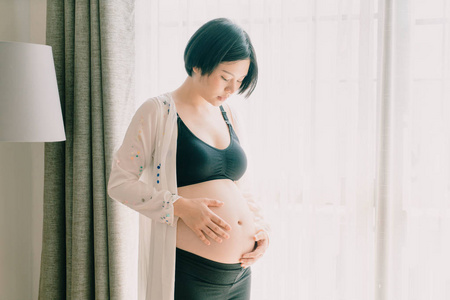 年轻美丽的亚洲孕妇抚摸她的腹部在家里
