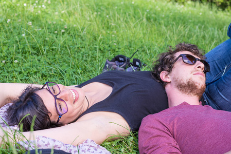 一对年轻的情侣躺在公园里郁郁葱葱的青草上, 放松, 拥抱。真正的人, 自然的颜色。Conpept 愉快的关系和夏天生活方式
