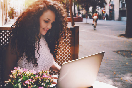 卷曲的黑发女孩在街边咖啡馆的笔记本电脑上工作