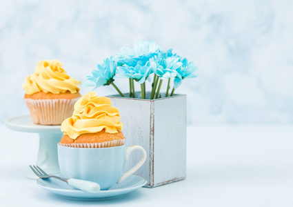 蛋糕与嫩黄色奶油装饰和蓝色菊花花束在复古破旧别致的花瓶在蓝色柔和的背景