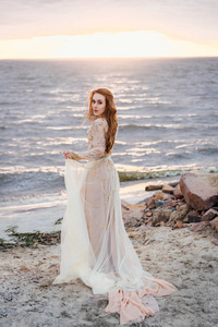 日落时分, 年轻漂亮女子在海边的婚纱礼服上摆造型