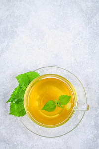 新鲜的绿荨麻叶和一个透明的玻璃杯草药荨麻茶在一个灰色的混凝土表。顶部视图