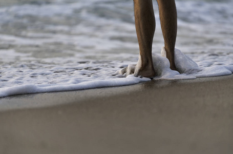人类的腿站在海滩上气泡波浪海