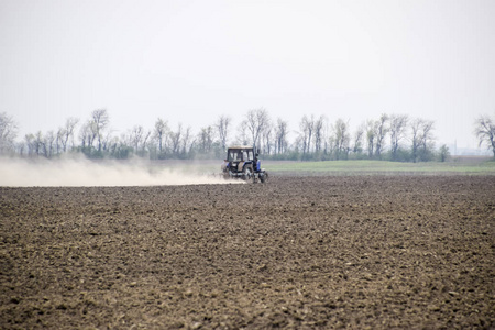 拖拉机耙在田野上的泥土, 并在它背后创造了一团尘埃。