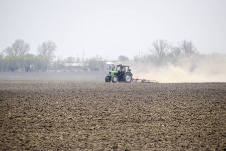 拖拉机耙在田野上的泥土, 并在它背后创造了一团尘埃。