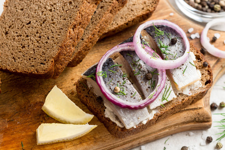 三明治配腌的鲱鱼 黄油和红洋葱在旧仿古砧板上