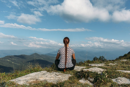 坐在岩石顶部与魔术山风景的年轻妇女冥想或做瑜伽