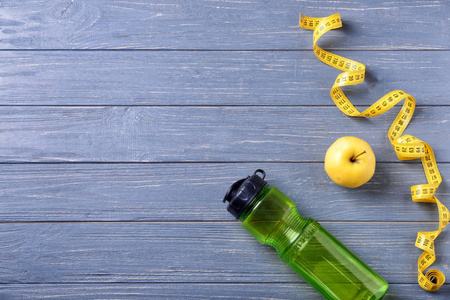 在木质背景下, 用瓶装水苹果和测量胶带平躺在一起。健身房锻炼