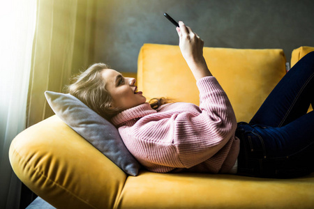 年轻妇女在她的智能手机上浏览互联网躺在家里的沙发上