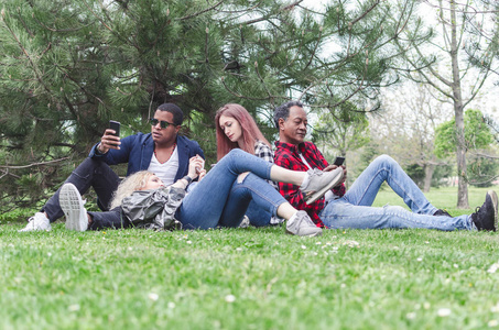 一群年轻人在公园里玩, 坐在草地上, 使用智能手机