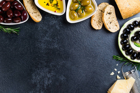 橄榄, ciabatta 面包, 乳酪, 油, 草本和香料在黑石头背景。地中海小吃。开胃菜 gourman 食物。复制空间