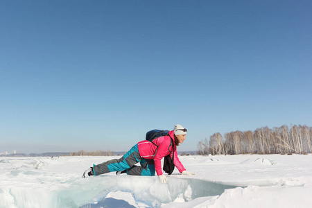 穿着红色夹克爬在结冰的河上的浮冰上的快乐女人