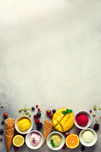 冰淇淋球在碗, 华夫饼锥, 浆果, 橙色, 芒果, 开心果在灰色的具体背景。多彩的收藏, 平坦的布局, 夏日的概念, 顶部视图