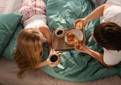 年轻可爱的夫妇在床上吃早餐