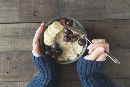 健康的早餐。有麦片粥和水果的灰色碗在妇女的手。饮食食品概念