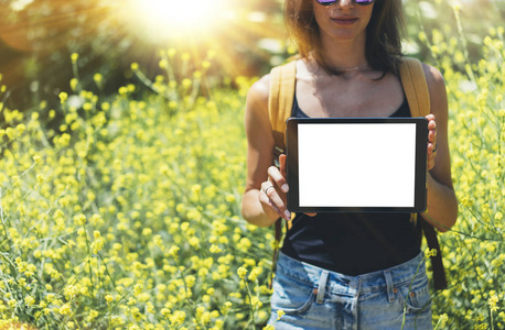 自然观赶时髦的人拿在手里的平板电脑。在太阳耀斑和黄色鲜花背景，文本，女摄影师的空白空屏幕复制空间的样机上使用小工具的女孩旅行者
