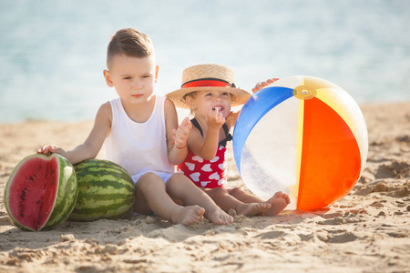 男孩和女孩坐与西瓜在海滩附近水