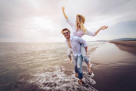 快乐的情侣在沙滩上享受夏日的假期。快乐的女孩背负着年轻的男友玩得开心