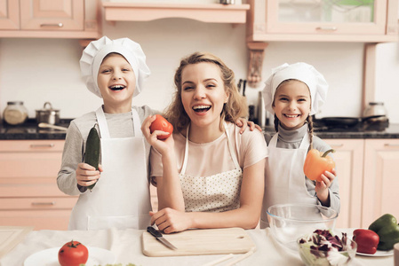 儿童在白色帽子和母亲拿着蔬菜沙拉在厨房