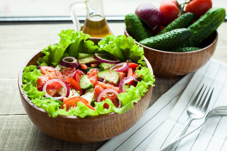 仿古沙拉的新鲜的西红柿，黄瓜，红洋葱和生菜，穿着用橄榄油和胡椒粉一个木碗。顶视图