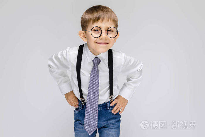 在灰色背景下戴眼镜的可爱严肃自信的小男孩肖像