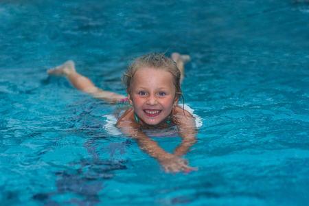 小女孩学习在大体育游泳池里游泳。小儿童游泳学校。健康的孩子享受积极的生活方式。学龄前儿童练习用泡沫垫