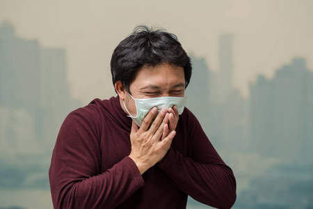 亚洲男子戴口罩反对空气污染与咳嗽在高公寓阳台, 可以看到污染和大雾的曼谷城市景观背景, 医疗保健理念