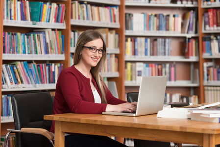 快乐的女学生在图书馆中的笔记本电脑