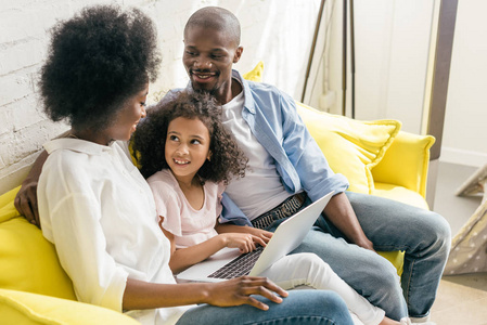 非洲裔美国人家庭与膝上型电脑在沙发上休息在家