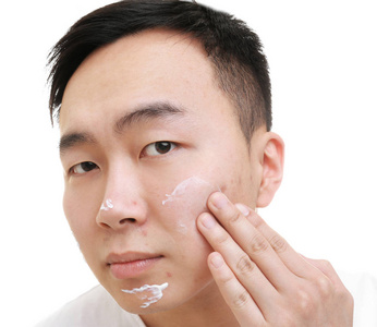 应用对问题肌肤均匀涂于面部，奶油白色背景上的亚洲年轻男子