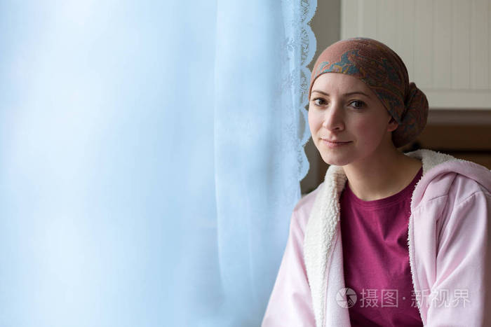 年轻阳性的成年女性癌症患者坐在厨房的窗口 微笑着看着相机