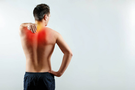 一个男人握着他的手, 肩膀受伤了, 肩膀上的疼痛用红色突出了。光背景。医学的概念图片