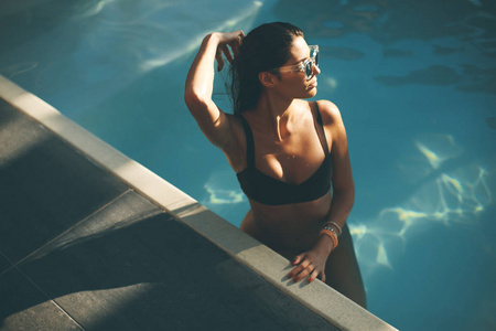 年轻苗条的妇女在炎热的夏日里在游泳池边放松身心