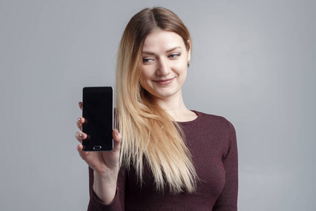 关闭一个微笑的女人显示屏幕移动电话, 而站在灰色背景隔离的肖像