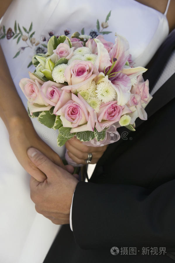 新婚夫妇在海滩上散步时手牵着手海滩上带花束的新郎新娘(特写)新郎戴