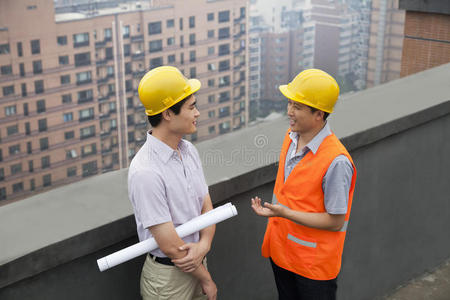 建筑师和建筑工人在屋顶上交谈，手捧蓝图，北京