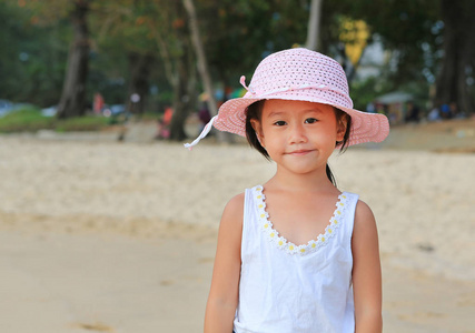 可爱的小亚洲女孩的肖像戴草帽在海滩上看着相机