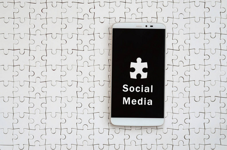 一个带有触摸屏的现代大智能手机坐落在一个白色拼图拼图在组装状态与题字。社会媒体