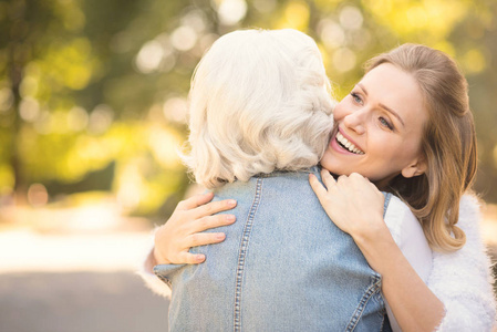 微笑的年轻妇女拥抱老母亲在公园里