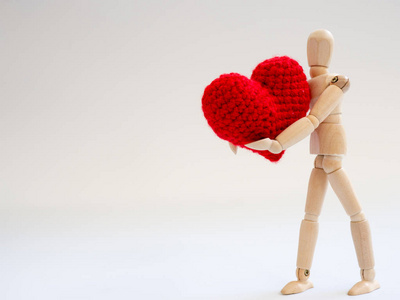 木制木偶站在白色屏幕背景上, 手持一颗红色的心。木制木偶抱着爱与关怀的心