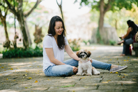 一个年轻的泛亚洲妇女的肖像坐在她年轻的石 tzuh 小狗在公园里的一天。她在微笑, 他们都在享受温暖的一天。