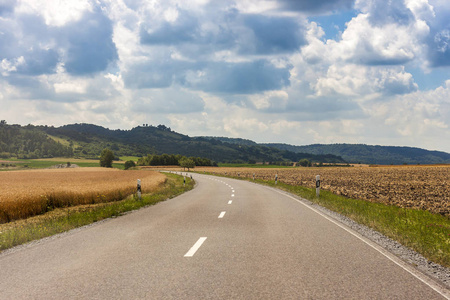 国家农村柏油路在德国通过绿色的田野和云在蔚蓝的天空，在夏季的一天