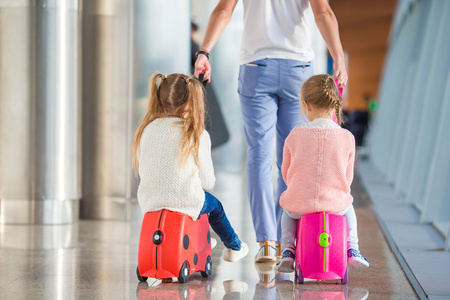 可爱的小女孩，和父亲一起在机场坐上等待登机的行李箱