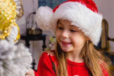 可爱的快乐女孩，在红色的帽子挂在圣诞树上的装饰