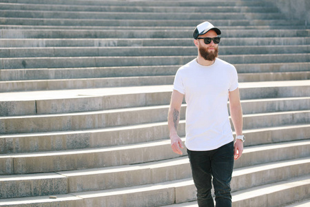 时髦英俊的男性模特与胡子穿着白色空白 t恤和棒球帽与空间为您的标志或设计在休闲城市风格